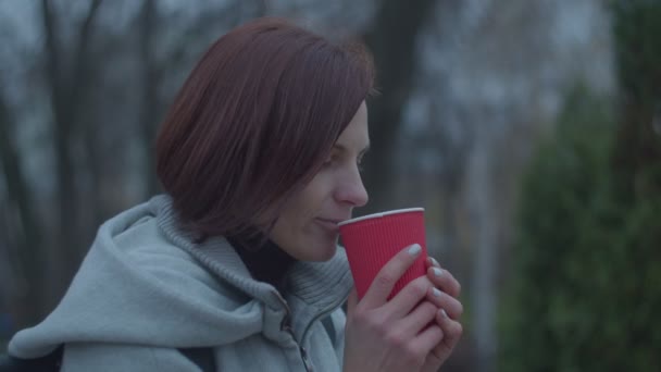 Jonge vrouwen die hete koffie of thee drinken in rode papieren beker op winderige straat. Vrouw het gevoel koud en het houden van hete kop koffie in handen. — Stockvideo