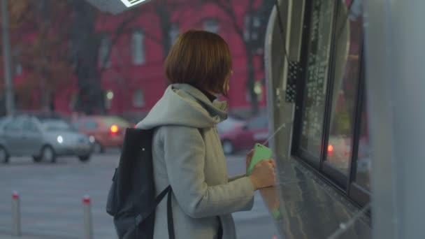 Junge brünette Frau mit Rucksack kauft heißes Kaffeegetränk beim Streetfood-Truck. Frau wird kalt, während sie auf der Straße auf Tee wartet. — Stockvideo