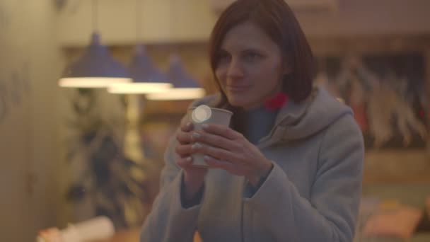 Junge Frauen im Mantel trinken Kaffee im Café, Fensterbild in Zeitlupe. Diaaufnahme von Händen, die weiblichen Lippen eine Tasse Tee reichen. — Stockvideo