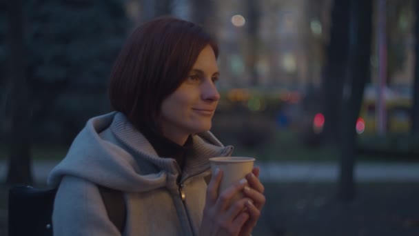 Unga vuxna kvinnor dricker varmt kaffe eller te i pappersmugg på suddig gata. Kvinna fryser och håller varm kopp kaffe i händerna. — Stockvideo