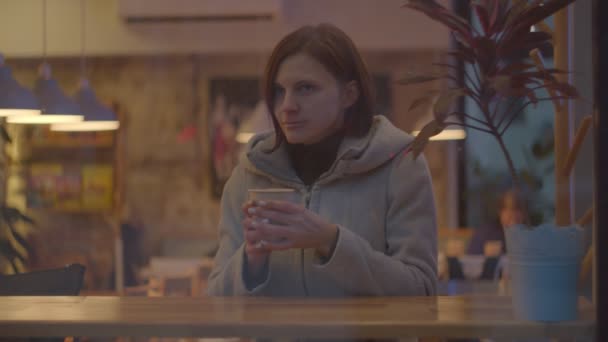 Unga kvinnor i rock dricker kaffe på kafé, fönster skjutna i slow motion. Kvinna som sitter vid fönstret i kaffeshop med kopp dryck. — Stockvideo