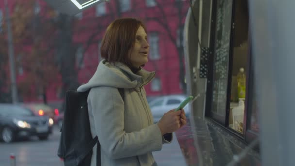 Νεαρή μελαχρινή γυναίκα με σακίδιο αγοράζοντας ζεστό καφέ ποτό στο δρόμο φορτηγό τροφίμων. Γυναίκα αισθάνεται κρύο, ενώ περιμένει για τσάι στο δρόμο. — Αρχείο Βίντεο