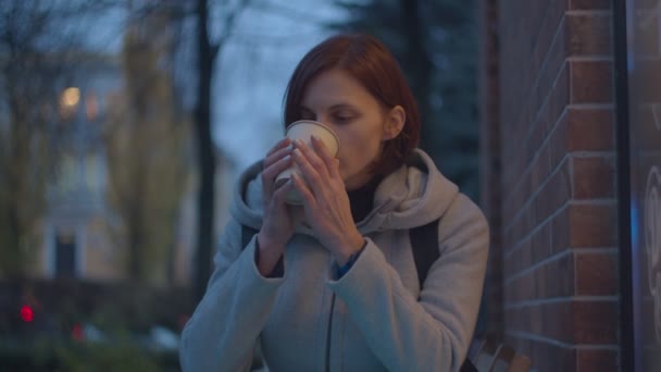 Jonge volwassen vrouwen die hete koffie of thee drinken in papieren bekertje op wazig straatje. Vrouw het gevoel koud en het houden van hete kop koffie in handen. — Stockvideo