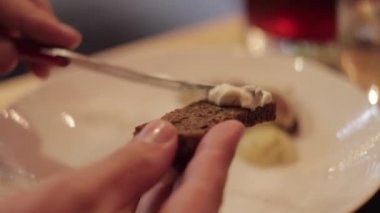 Farklı aperatifleri olan bir parça ekmek bıçakla yayılıyor. Kadın elleri restoranda ekmeğe tereyağı sürüyor.. 