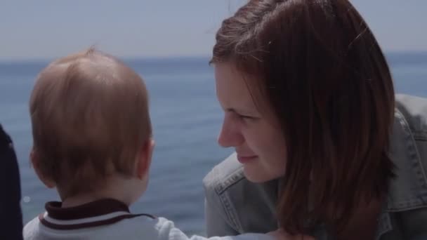 Le nouveau-né touche les cheveux de sa mère et regarde vers la mer. Brunette maman avec enfant au bord de la mer . — Video