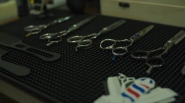 Berber makası, üzerinde berber logosu olan kauçuk paspasın üzerinde yatıyor. Masada farklı berber aletleri var.. 