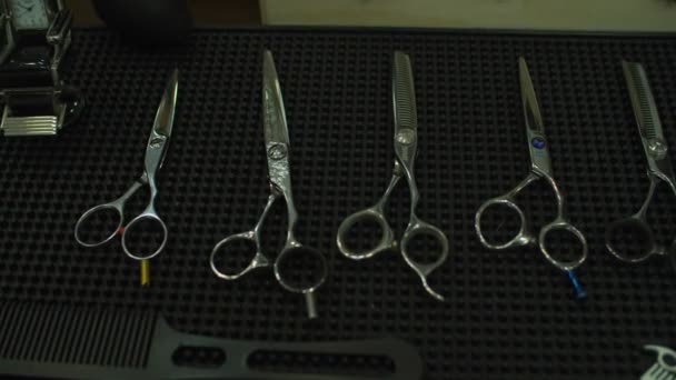 Tijeras de peluquería colocadas en una alfombra de goma con el logotipo de la barbería. Diferentes herramientas de peluquería sobre la mesa . — Vídeos de Stock