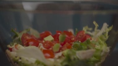 Dilimlenmiş avokado, domatesli taze salata ve yavaş çekimde tavukla cam kaseye uçuyor. Salata yapma süreci. 