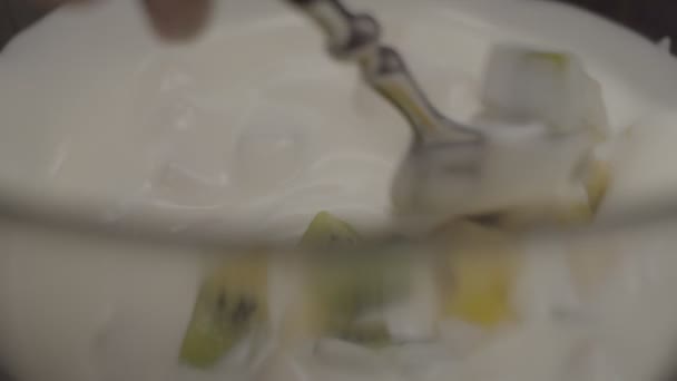 Frutas cortadas en rodajas que caen en yogur blanco en cámara lenta. Plátano picado, kiwi y piña mezclados en yogur cremoso junto a la cuchara . — Vídeo de stock