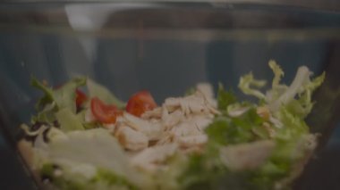 Dilimlenmiş domatesler yavaş çekimde taze salatayla cam kaseye uçuyor. Salata yapma süreci. 