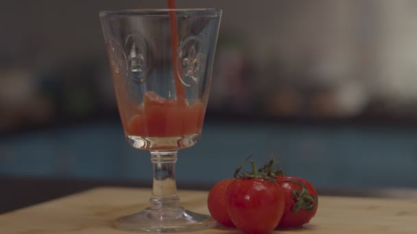 Stemmed glass is filled with red tomato juice with 3 tomatoes lying on the wooden cutting board in slow motion. — Stock Video