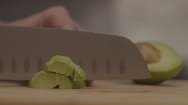 Женские руки нарезают авокадо большим кухонным ножом на деревянной доске в замедленной съемке. Половина авокадо с ямой . — стоковое видео