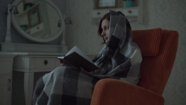 Ung kvinna i rutig läsa papper bok sitter i mysig orange fåtölj i sovrummet. Kvinnlig läsning och vändning sidor i boken i slow motion. — Stockvideo