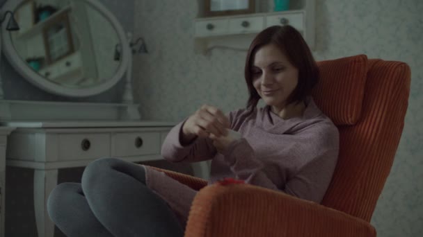 Jeune femme heureuse avec ses nouvelles montres intelligentes assises dans un confortable fauteuil orange dans la chambre. Femme bénéficiant d'un nouveau bracelet sur son gadget intelligent à portée de main . — Video