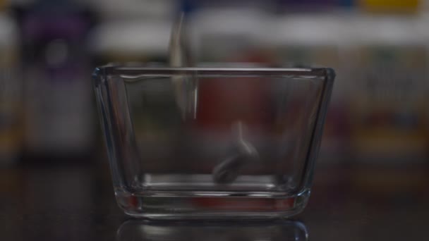 Primer plano de diferentes cápsulas y píldoras que caen en un recipiente de vidrio con botellas de vitaminas borrosas detrás en cámara lenta. Concepto sanitario . — Vídeo de stock