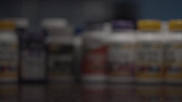 Close up of different capsules and pills falling into glass bowl with vitamins bottles blurred behind in slow motion. Healthcare concept. — Stock Video