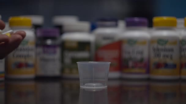 Close up of different capsules and pills falling into glass bowl with vitamins bottles blurred behind in slow motion. Healthcare concept. — Stock Video