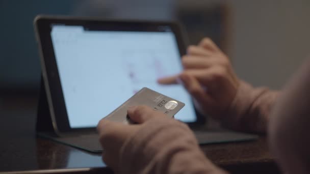 Manos femeninas sosteniendo la tarjeta de débito y haciendo compras en línea en la computadora tableta. Mujer elegir vestidos en la tienda de Internet y hacer la compra en cámara lenta . — Vídeo de stock