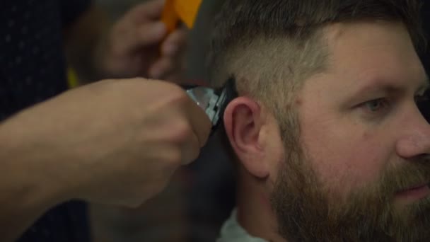 Barbeiro fazendo corte de cabelo para o homem da barba na capa de cabeleireiro por máquina de barbear elétrica e pentear na barbearia em câmera lenta . — Vídeo de Stock