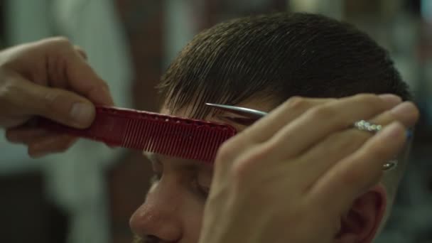 Corte de pelo para hombre por tijeras barberos y peine con el logotipo de la barbería detrás en cámara lenta. Manos de hombre haciendo corte de pelo masculino en el salón . — Vídeo de stock