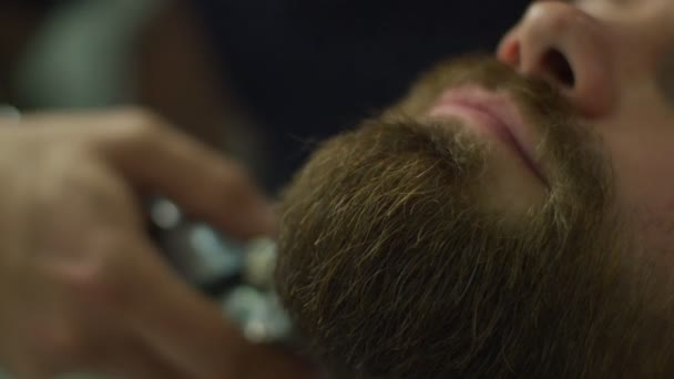 Homem barbudo e barbeiros mãos barbear barba por máquina de barbear elétrica e pentear em câmera lenta. Masculino com olhos fechados na barbearia . — Vídeo de Stock