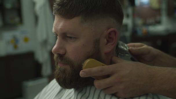 Barberare hand rakning mans huvud av elektrisk rakmaskin, sida visa i slow motion. Man med skägg i frisörsalongen — Stockvideo