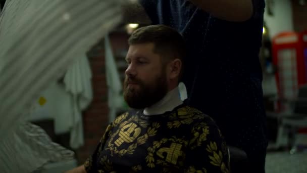 Barbeiro levando capa de barbeiro em homem com barbas e cabelo na barbearia em câmera lenta . — Vídeo de Stock