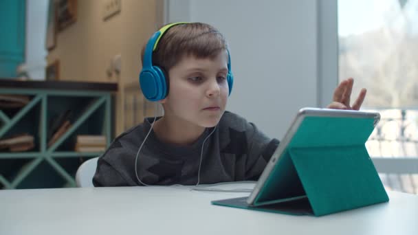 Niño de la escuela con autismo jugando en el ordenador tableta en auriculares de color. Niño tocando la pantalla del gadget y mirando a la cámara en cámara lenta . — Vídeos de Stock