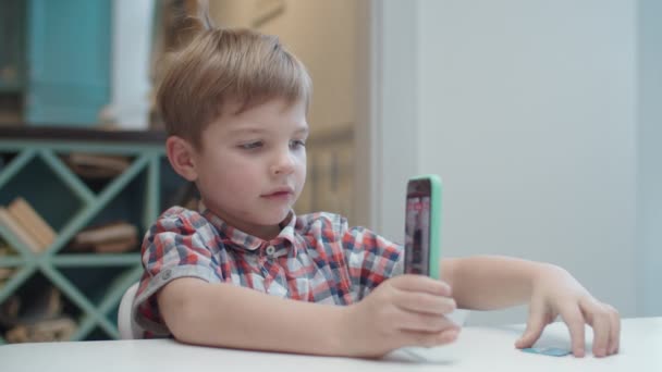 Przedszkolak trzymający smartfona w rękach i robiący zdjęcie karty do aplikacji rozszerzonej rzeczywistości. Kid lubi gry Ar. — Wideo stockowe