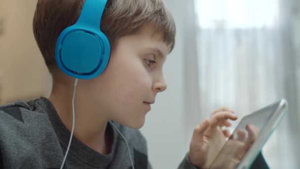 Närbild av skolpojke med autism spelar på surfplatta dator i färg hörlurar. Kid vidröra gadget skärm med reflektion i slow motion. — Stockvideo