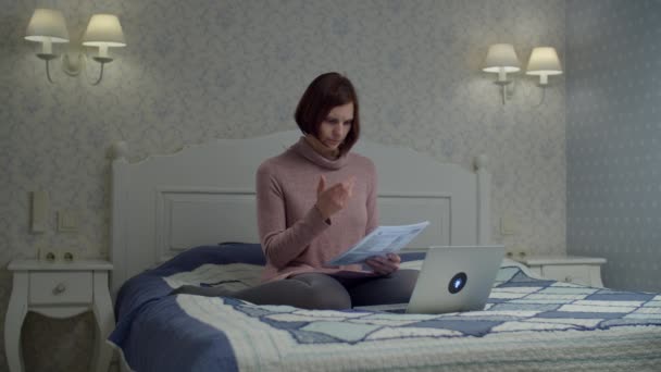 Brunett kvinna i klänning med papper dokument sitter på sängen. Kvinnliga studerar räkningar och ropar på hjälp. — Stockvideo