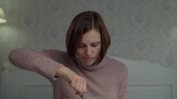 Mujer morena llorona comiendo vainilla y cubo de helado de chocolate sosteniendo las manos sentadas en la cama. Mujeres disgustadas comiendo dulces . — Vídeos de Stock