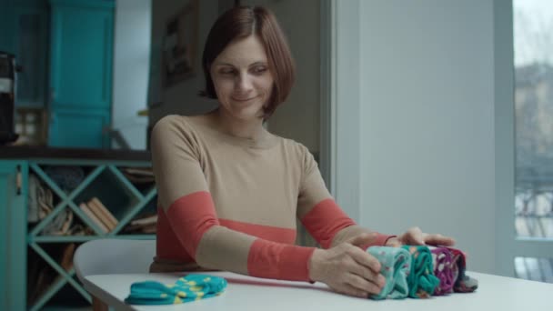 Giovane donna adulta sorridente che piega i calzini a colori seduta a tavola. Marie Kondo metodo di organizzazione e semplificazione della casa . — Video Stock