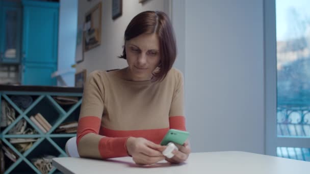 Young female brunette receiving income call by wireless earphones sitting at the table. Woman smiling and talking by earphones. — 图库视频影像