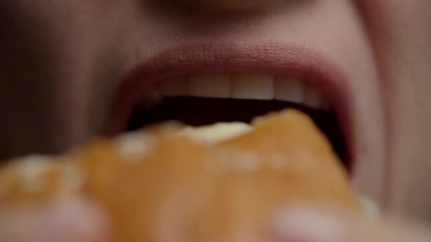 Macro primer plano de la boca femenina comiendo hamburguesa con queso en cámara lenta. Bollo de hamburguesa mordida mujer con semillas de sésamo . — Vídeo de stock