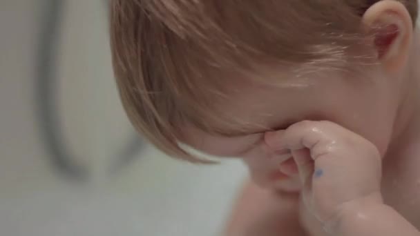 Niño rubio tomando un baño y frotándose los ojos con las manos. Baño infantil . — Vídeos de Stock