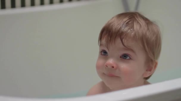 Niño rubio bebé tomando un baño con paño. El bebé se levanta y se levanta con las manos pequeñas saludando a mamá. Hijo feliz de ver a madre . — Vídeo de stock