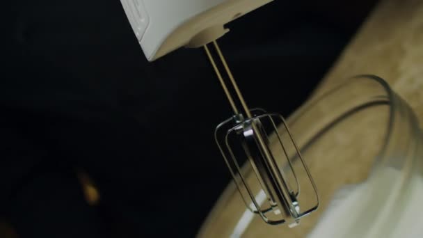 Close up of blender whisking eggs into mousse in glass bowl in slow motion with blurred light behind. — Stock Video