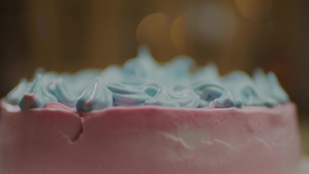 Περιστρεφόμενο ροζ κέικ με μπλε διακοσμημένο λουλούδι μαρέγκας σε αργή κίνηση με θολή φώτα φόντου. — Αρχείο Βίντεο