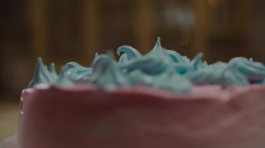 Mavi süslemeli pembe pasta yavaş çekimde bulanık arka plan ışıklarıyla dönüyor.. 