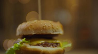 Köfteli döner burger, erimiş peynir, domates, salatalık ve salata yaprakları yavaş çekimde bulanık arka plan ışıkları.