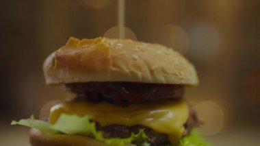 Köfteli döner burger, erimiş peynir, domates, salatalık ve salata yaprakları yavaş çekimde bulanık arka plan ışıkları.