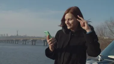 Gülen 30 'lu yaşlardaki kadın araba kaputunda siyah bir ceket içinde elinde akıllı telefonuyla Falls River manzarasıyla dans ediyor.. 