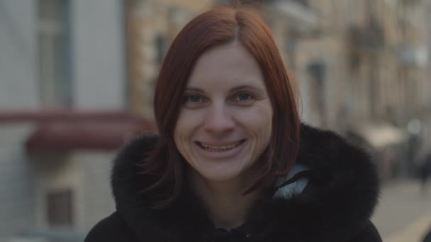 Portrait of 30s brunette female adult in black coat smiling to camera at the city street in cold windy weather. — 비디오