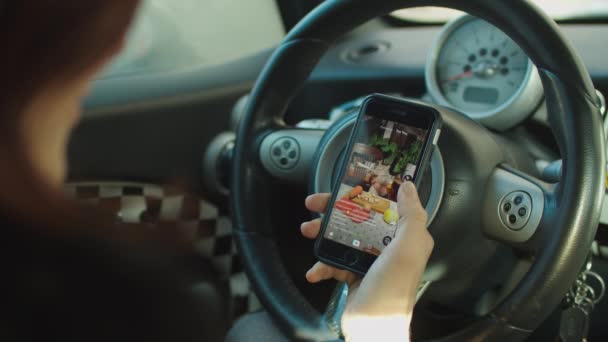 女性の手は車の中でガジェットを使用して、指はスマートフォン上でソーシャルメディアタイムラインをスクロールします。お気に入りと共有オンライン. — ストック動画