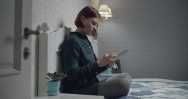 Genç, esmer, yetişkin bir kadın tablet bilgisayarda çalışıyor. Yatakta oturuyor. Aletle belgelerin resmini yapan kadın. 