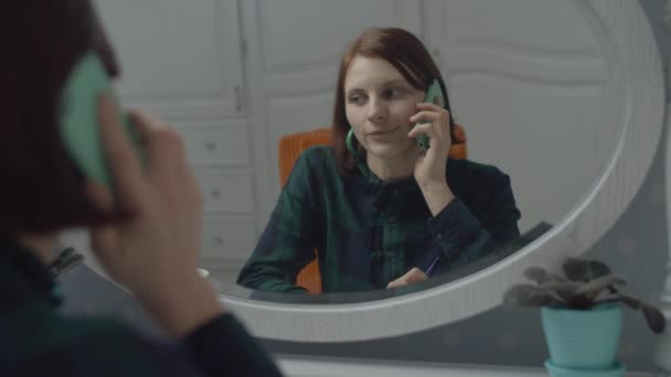 Young female adult talking by cell in mirror reflection in slow motion. Woman smiling with smartphone in hands. — Stock Video