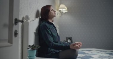 Nilüfer pozisyonunda oturan genç bir kadın yatağın üzerinde taşınabilir uygulamalarla meditasyon yapıyordu. Akşamları meditasyon yaparken kendini huzurlu hisseden kadın.. 
