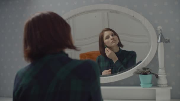 Young female adult putting on earrings in mirror reflection in slow motion. Women smiling sitting at bedroom. — Stock Video