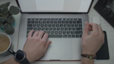 Dizüstü bilgisayarda yazan ve kahve içen erkek elleri. Eller klavyede çalışıyor. Dizüstü bilgisayar, akıllı telefon, kulaklık ve bir fincan kahve.. 